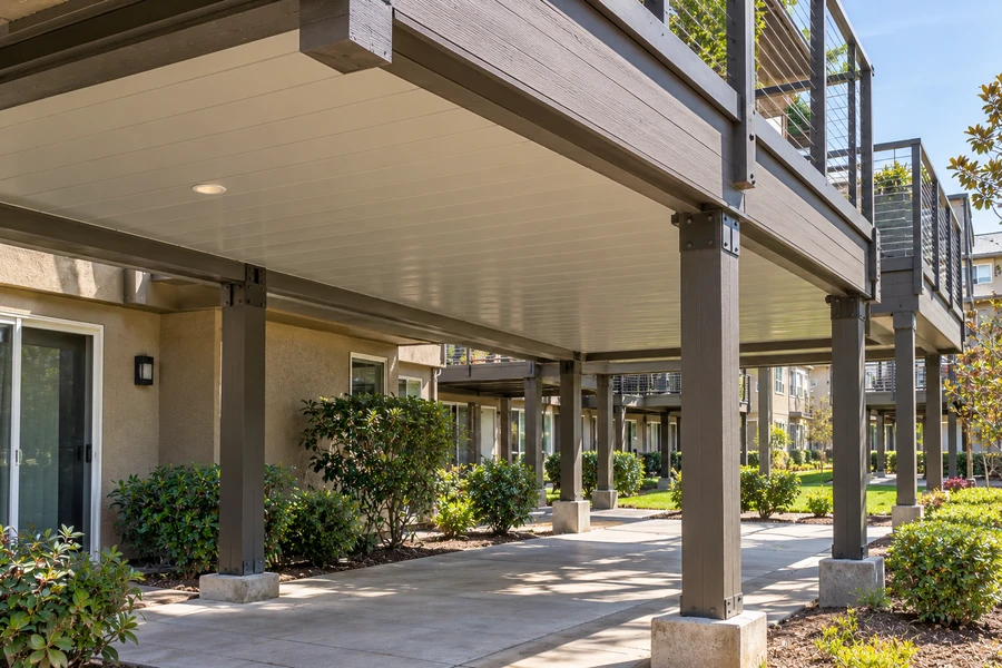 Composite deck and stair run with the underside finished and lit, apartment community beyond