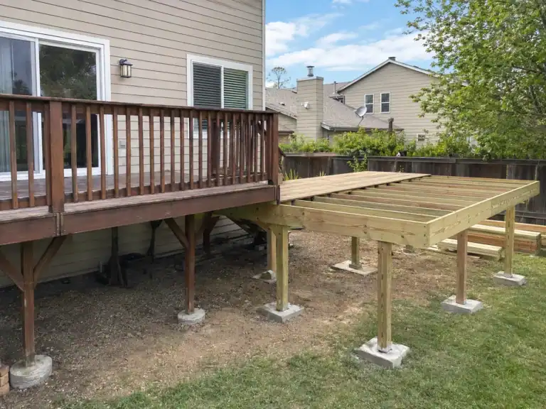 Deck extension in progress, new pressure-treated framing on fresh piers joining an older dark deck