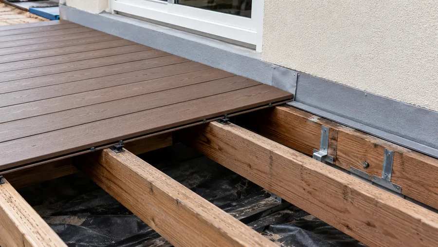 New composite decking going down over an existing frame, with the ledger flashed at the wall