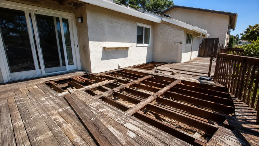 Deck partly stripped with old joists exposed and sections of framing removed for replacement