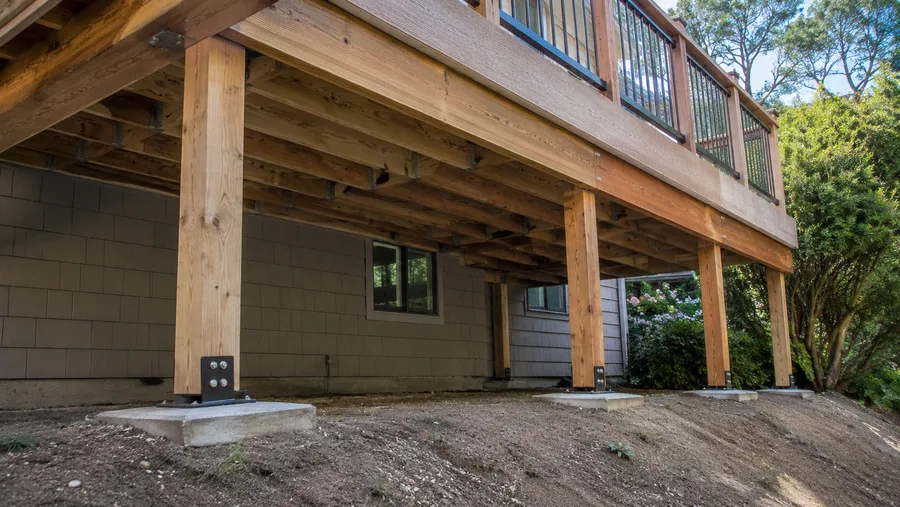 Underside of a rebuilt deck showing new posts on concrete pads with metal bases