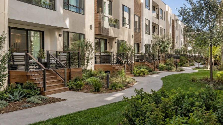 Row of wood entry decks with short stairs and black metal railings along a landscaped walkway