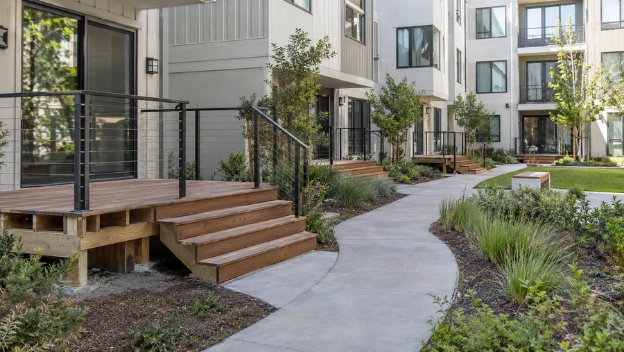 Wood deck and four-step stairs with cable railing along a courtyard walkway at a multi-story building