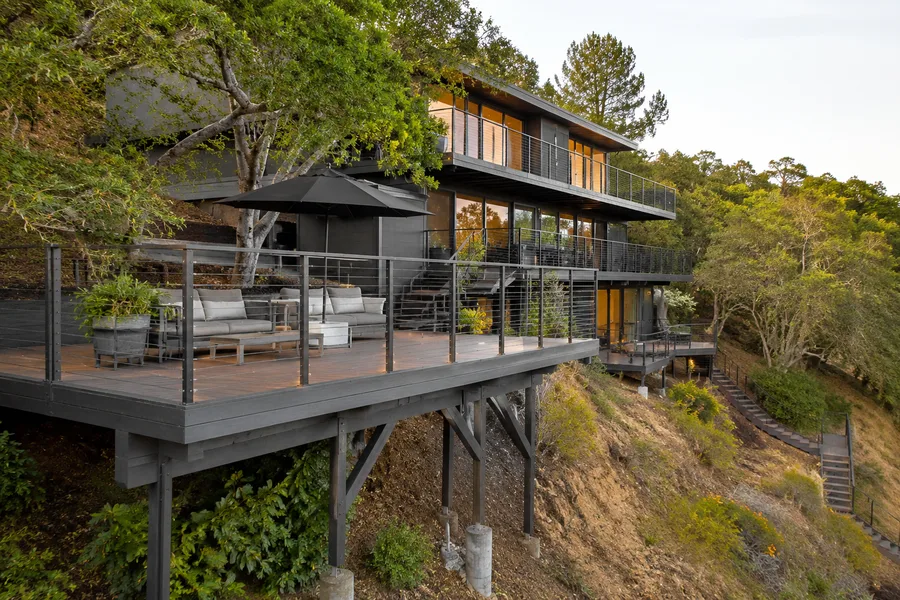 Multi-story hillside home with decks cantilevered on steel posts, and an exterior staircase descending the slope