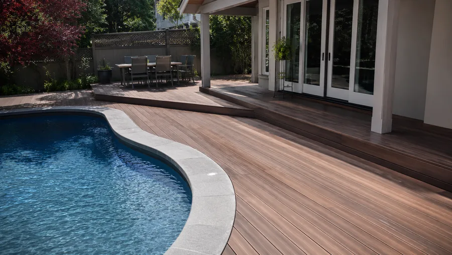Hardwood pool decking curving around an in-ground pool with a stone coping band