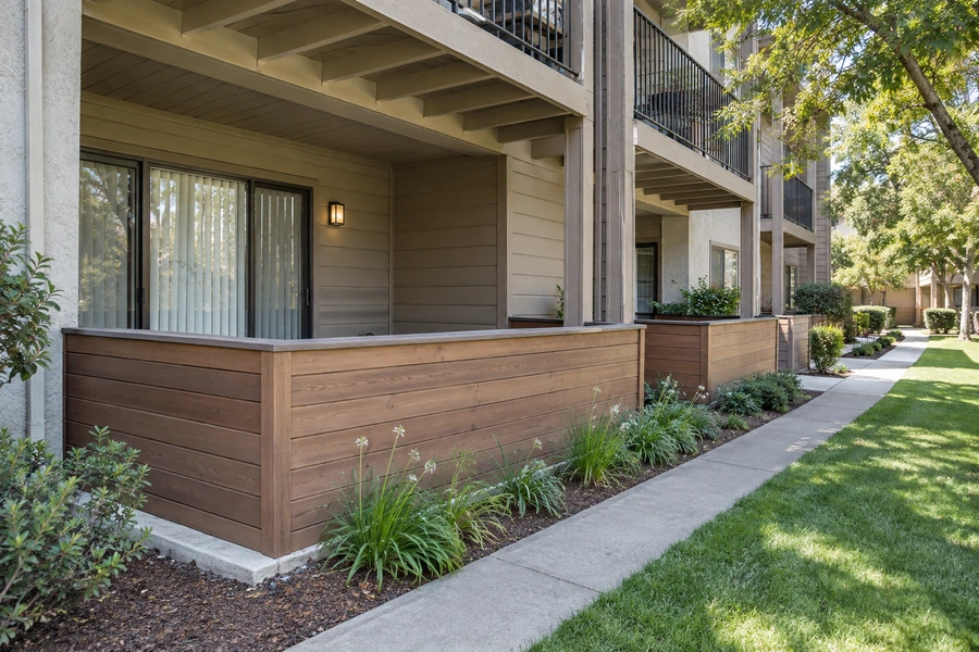 Covered ground floor patio with a horizontal wood privacy wall under an upper balcony at a multi story building