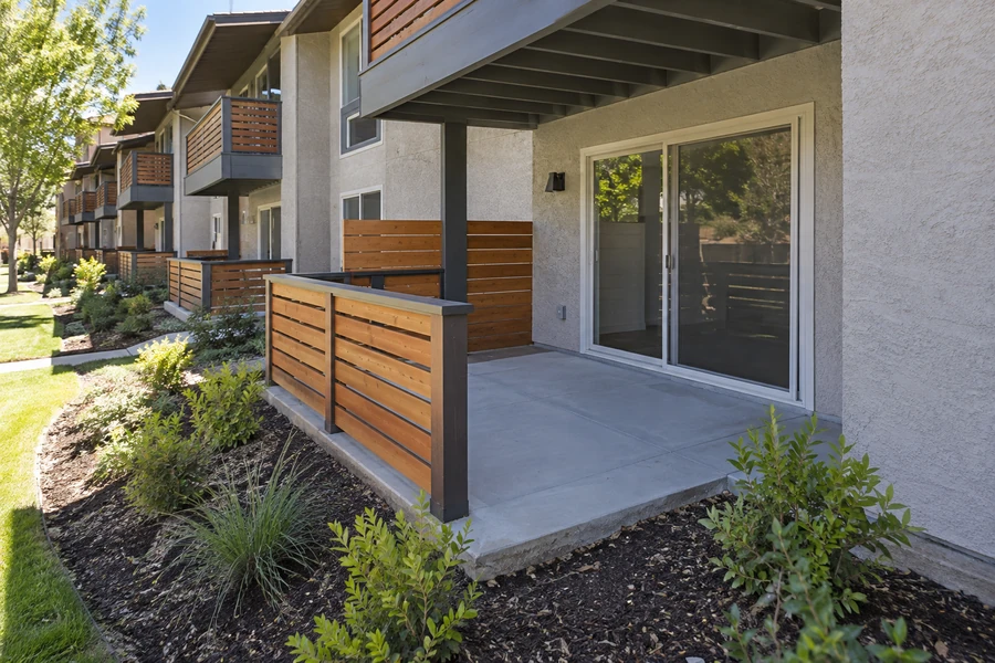 Concrete ground floor patio with wood slat railing and dark posts under an upper balcony