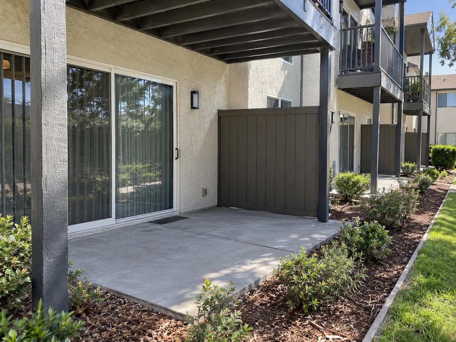 Concrete patio slab with a dark vertical board privacy screen under an upper balcony