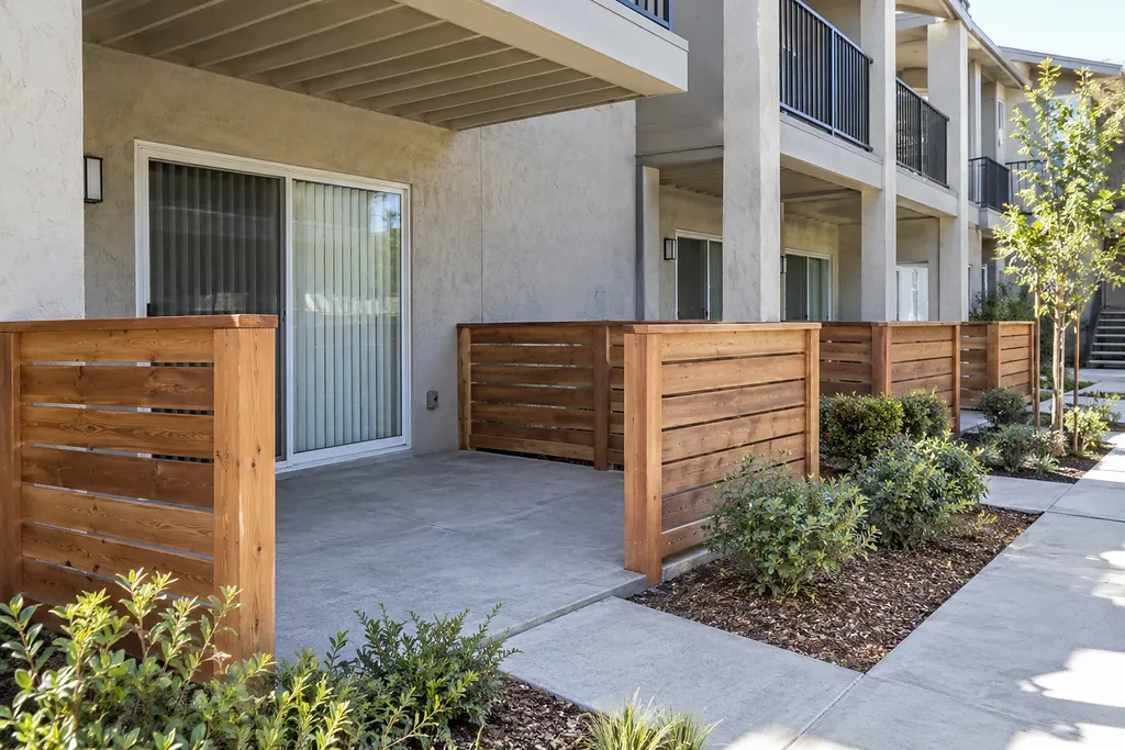 Row of concrete ground floor patios with wood slat privacy fences along a walkway at a multi story building