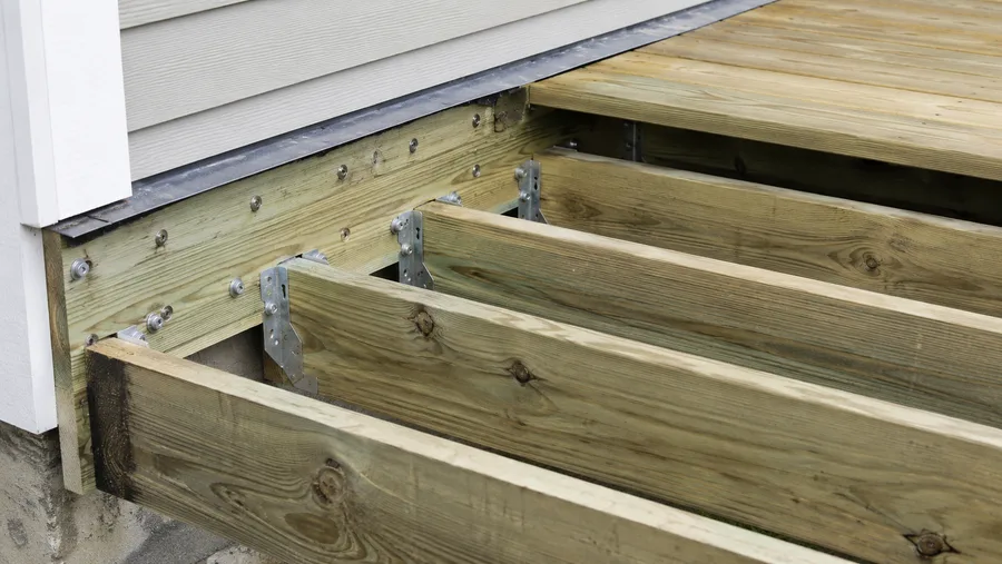 Pressure-treated ledger bolted to the wall with flashing over it and joist hangers set