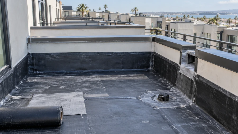 Waterproofing membrane being rolled out across a roof deck, with the drain, scupper and parapet already detailed