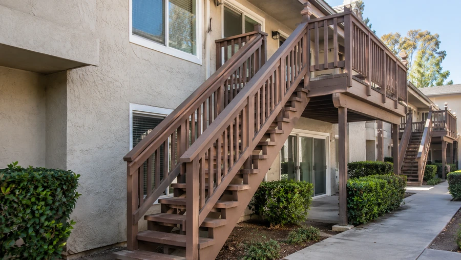 Long stair run and landing connecting a ground path to an upper-floor apartment balcony