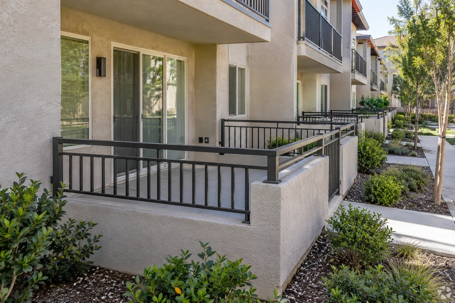 Ground-floor terrace with black picket guardrail on a concrete slab at a multi-story multi-unit building