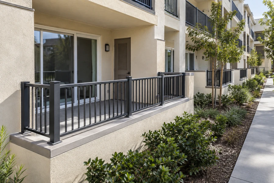 Concrete terrace with black metal picket railing along the ground floor of a multi-story multi-unit building