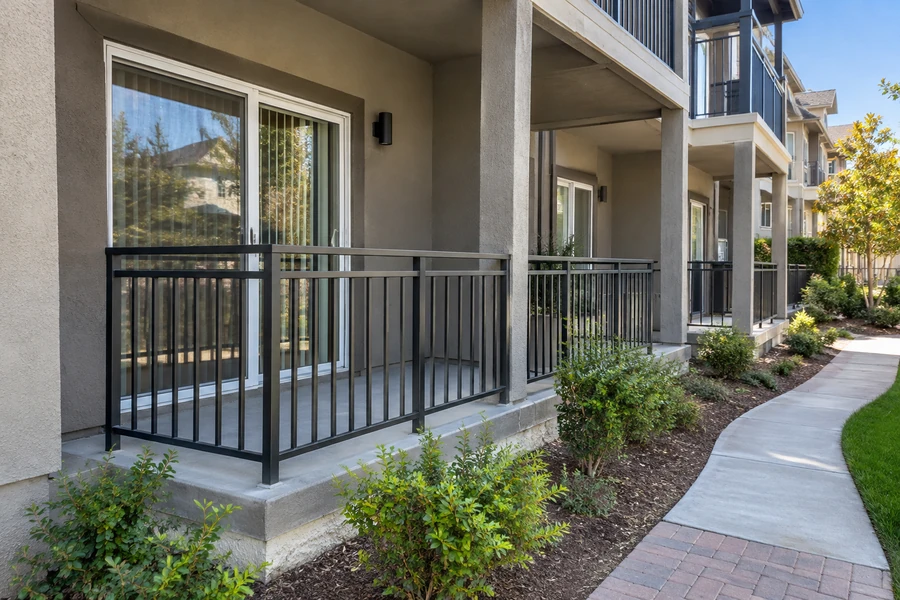 Ground-floor concrete terrace with black picket guardrail beneath stacked balconies of a multi-unit building