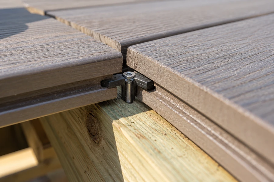Close-up of a hidden clip fastener screwed to a pressure-treated joist between the grooved edges of two composite deck boards
