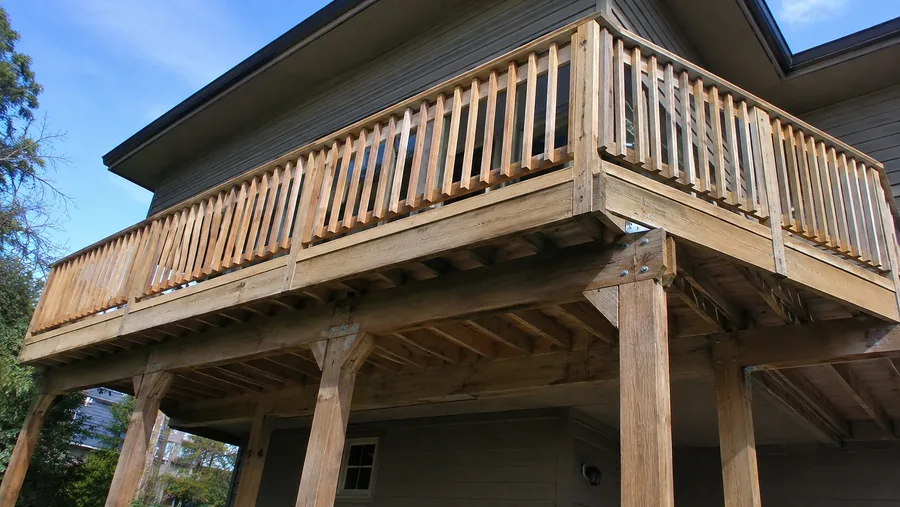 Wood balcony framing seen from below, with joists, knee braces and metal connectors at the posts