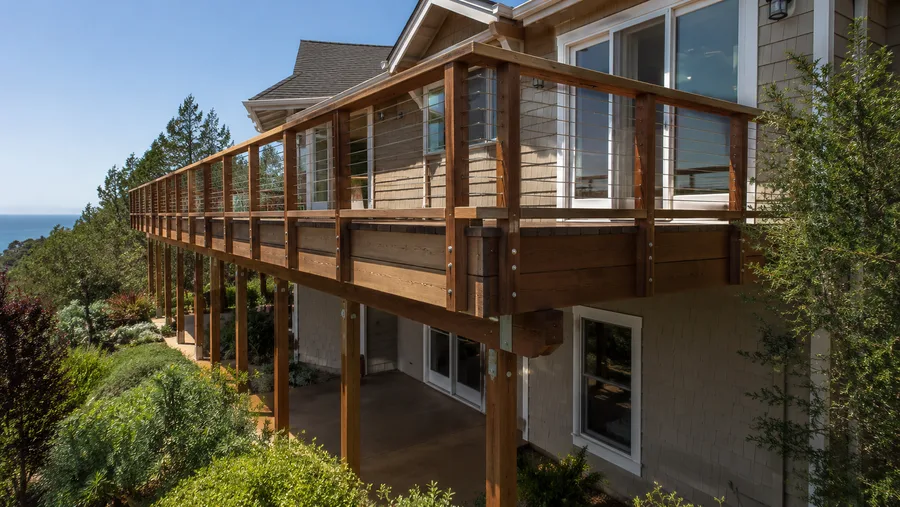 Long wooden balcony with timber posts and cable infill guardrails on a hillside property