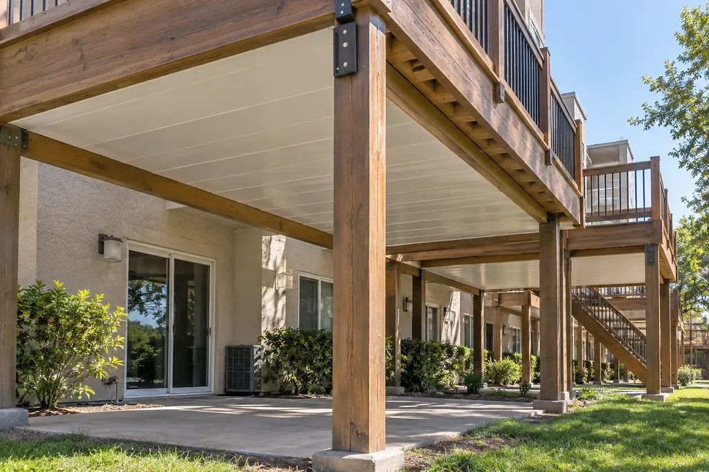 Timber deck structure on posts at an apartment community, seen from the covered space beneath