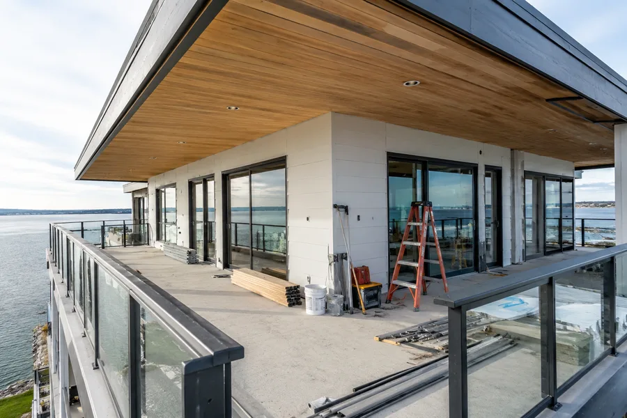 Wraparound balcony under construction on an upper floor, with glass guardrails installed